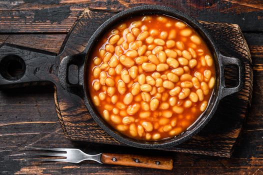 Beans in tomato sauce in a pan. Dark wooden background. top view