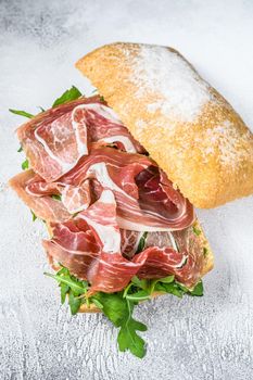 Prosciutto parma ham sandwich on ciabatta bread with arugula. White background. Top view