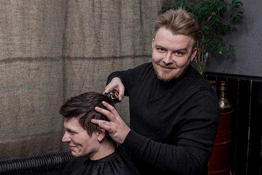 A positive barber or hairdresser of Caucasian appearance cuts the client of a guy with dark hair. Hairdressing