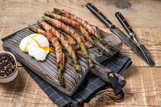 Roasted green asparagus wrapped in a bacon with egg. Wooden background. Top view
