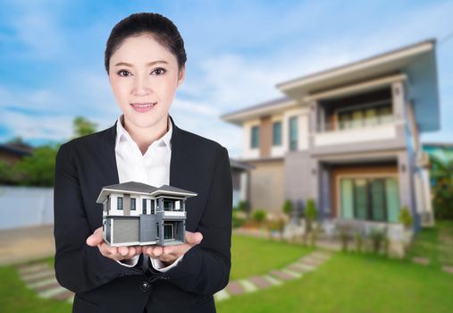 model house in business woman hand with actual house and garden 