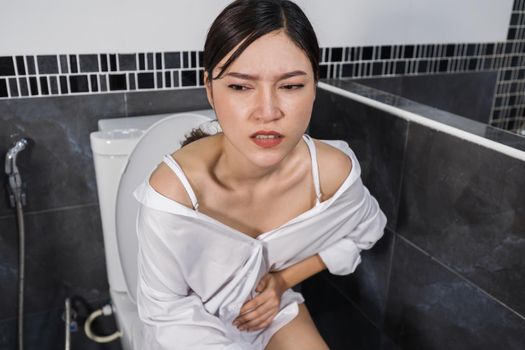 woman sitting on toilet and holding her painful Stomach
