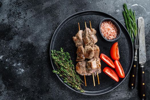 Shish kebabs grilled meat and vegetables on a plate. Black background. Top view. Copy space