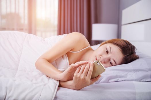woman using her smartphone on bed in bedroom with soft light