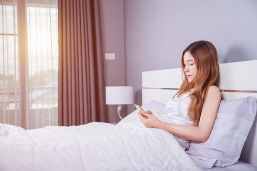 woman using her smartphone on bed in bedroom with soft light
