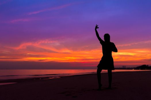 Silhouette of woman with hands up while standing on sea beach at sunset