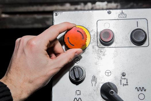 A man's hand turns the red button on an old industrial equipment control system