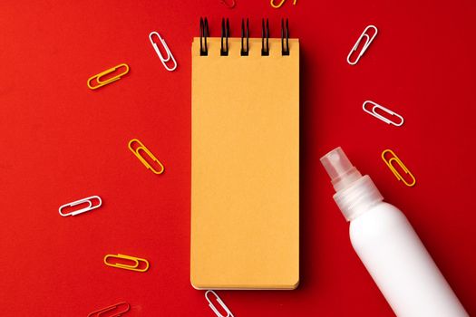 Small notepad with paper clips and spraybottle on red background