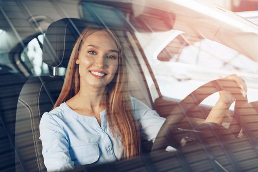 Attractive young woman sitting in new car in showroom