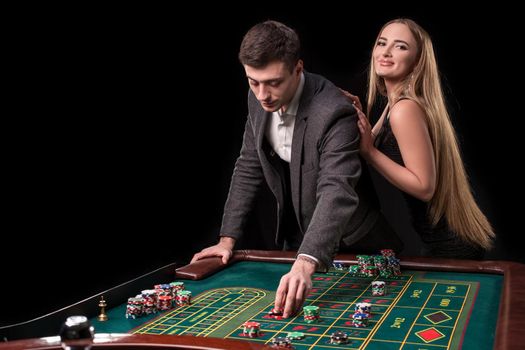 Elegant couple at the casino betting on the roulette, on a black background