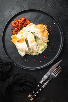Freshly cooked Chicken Kiev oozing garlic and parsley butter, with baked cherry tomatoes, mashed potatoes, on black stone background, top view flat lay