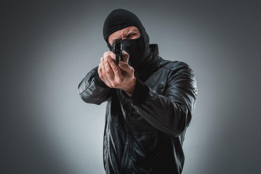 Burglar or terrorist in black mask shooting with gun.
