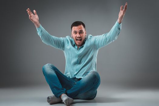 The man is sitting on the floor on gray background. Man showing different emotions.