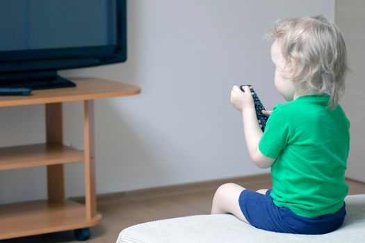 A child with a remote control in his hand turns on the TV to watch cartoons