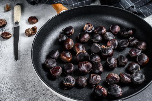 Roast chestnuts in a pan on a wooden table. White background. Top view