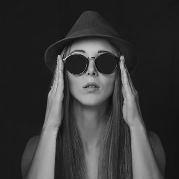 Beautiful girl with long hair in round sunglasses and hat. Fashion and beauty. Black and white image