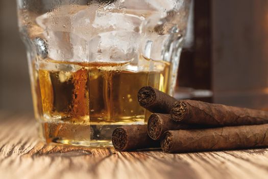 Glass of whiskey and rolled cigars on wooden table