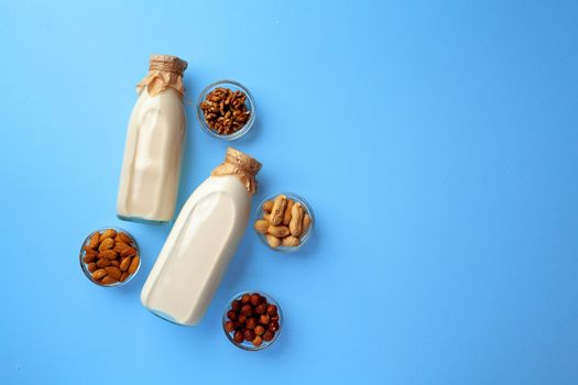 Bottles of vegan non dairy milk with various nuts on blue background