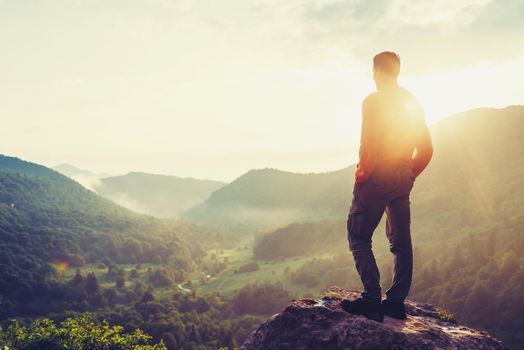 Traveler young man standing in the summer mountains at sunset and enjoying view of nature. Image with instagram color