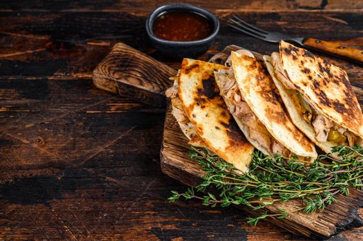 Mexican quesadilla with chicken, paprika, cheese and cilantro on wooden cutting board. Dark wooden background. Top view. Copy space