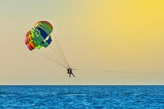 Man and woman tourists are flying on parasailing over the sea against the backdrop of the sunset sky and the horizon. Extreme vacation concept