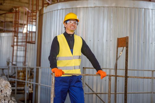 Cheerful man engineer standing near meta storage container at factory