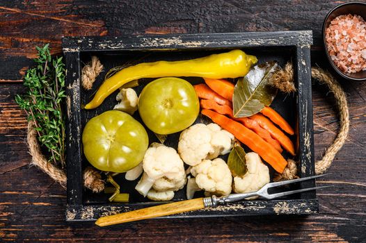Homemade marinated and pickles vegetables preserve on a wooden tray. Dark wooden background. Top view