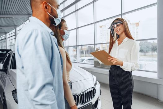 Woman car dealer consulting buyers wearing medical face shield