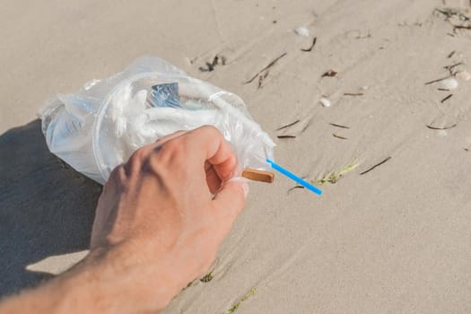 Man's hand picks up or collects garbage on a seaside beach close-up