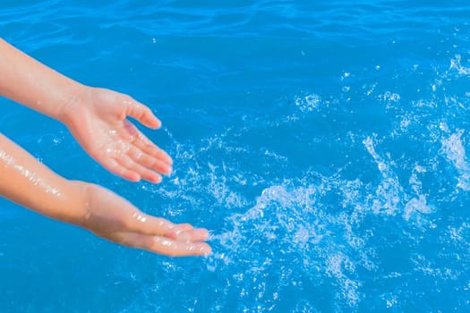 The hands of a young girl make splashes of blue pure sea water close-up