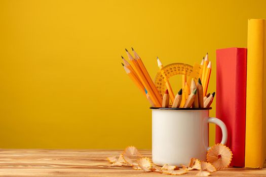 Metal cup with sharp pencils and pencil shavings on wooden desk