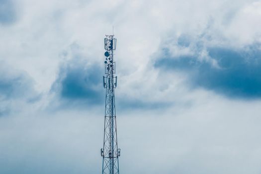 Cell tower telecommunications antena against the background of blue cloudy sky with clouds