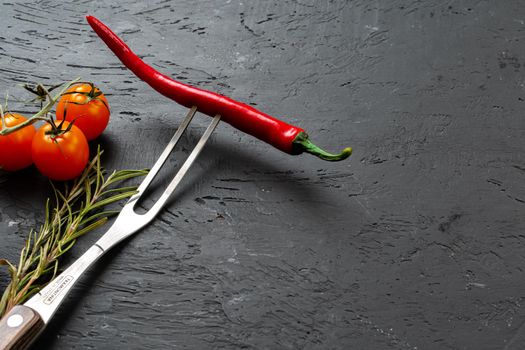Red chili pepper on fork on black stone background