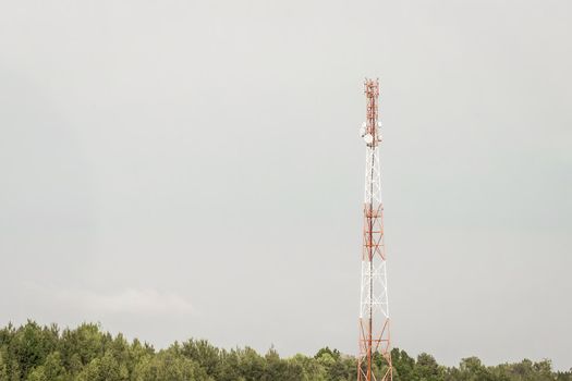 Telecommunication tower of mobile communication against the background of gray sky and trees