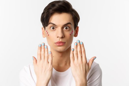 People, lgbtq and beauty concept. Beautiful gay man showing blue nail polish on fingernails and looking at camera, have manicure, standing over white background