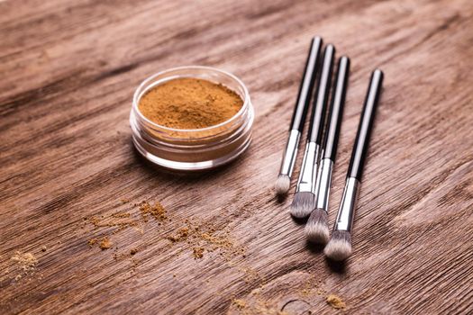 Loose compact mineral powder for face and a brushes for powder and visage on wooden background. Eco friendly and organic cosmetics.