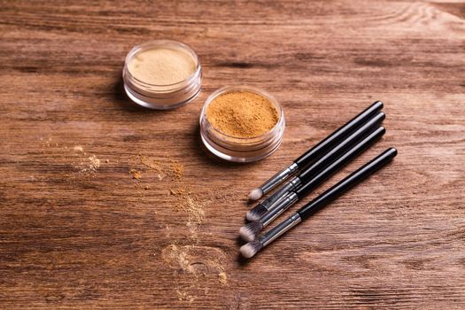 Loose compact mineral powder for face and a brushes for powder and visage on wooden background. Eco friendly and organic cosmetics.