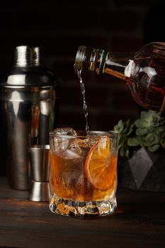 Old Fashioned cocktail in which whiskey is poured on a wooden background