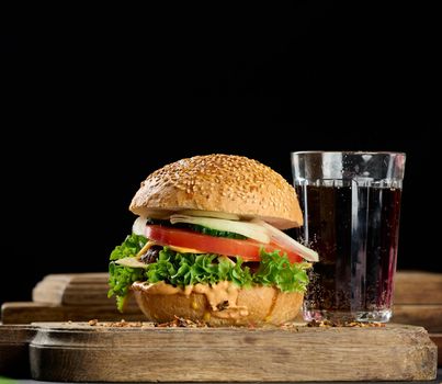 cheeseburger with grilled beef patty, cheddar cheese, tomato and lettuce on a wooden board, black background