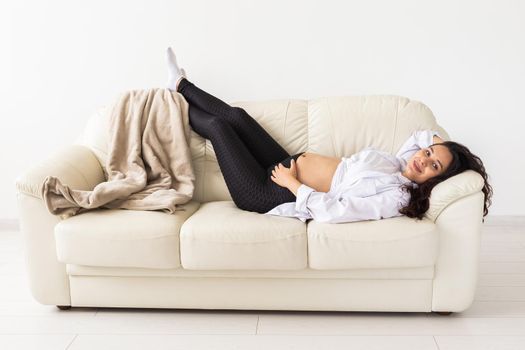 Hispanic pregnant woman lying on sofa at home. Pregnancy, resting and expectation concept.