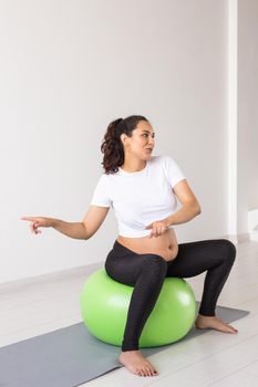 Cheerful pregnant woman dances while sitting on fitness ball. Well-being pregnancy, healthy lifestyle and positive concept.
