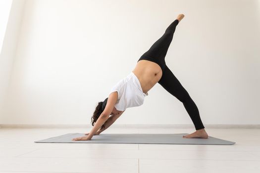 Young flexible pregnant woman doing gymnastics on rug on the floor on white background. Preparing the body for easy childbirth