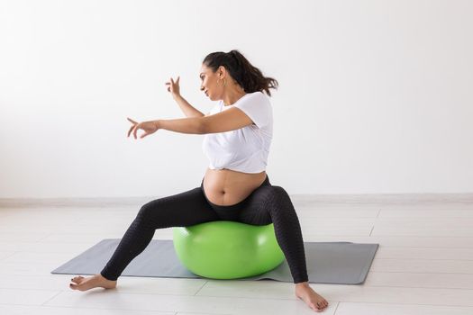Cheerful pregnant woman dances while sitting on fitness ball. Well-being pregnancy, healthy lifestyle and positive concept.
