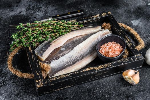 Fillet of Pickled marinated sea herring fish in a wooden tray. Black background. Top view