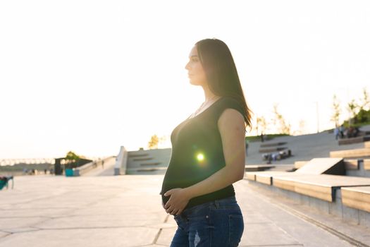 Pregnant hispanic woman on embankment, touching belly