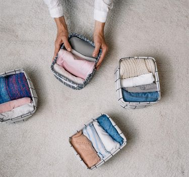 a neat housewife puts things in a laundry container during general cleaning with the help of a modern storage system. Top view The concept of a beautiful and comfortable organization