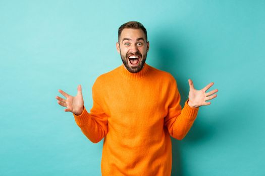 Image of happy and excited man announce big news, spread hands and shouting of joy, rejoicing, standing over light blue background