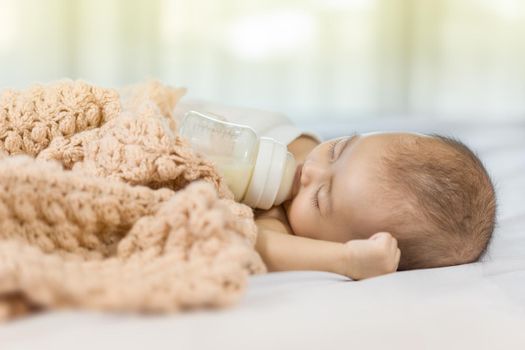 baby drinking milk from bottle and sleeping on bed