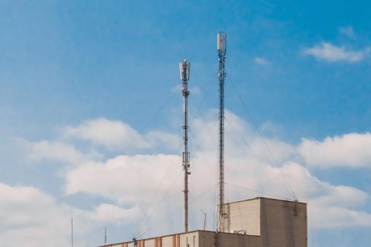 2 mobile cellular telecommunication antennas on the roof of a brick building against a blue sky
