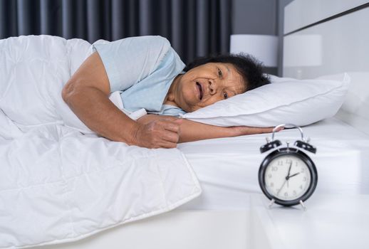 Old woman suffering from insomnia is trying to sleep in bed 